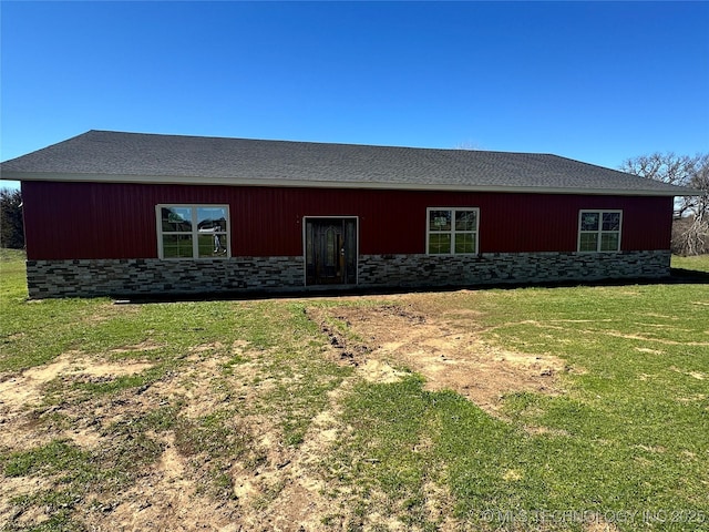 back of property featuring stone siding and a yard