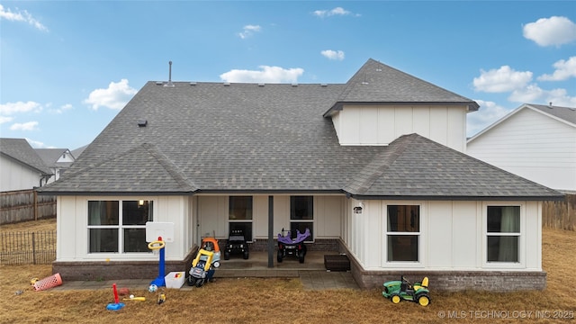 back of property with a patio, a shingled roof, brick siding, fence, and board and batten siding