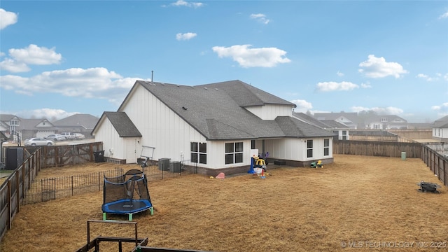 rear view of property featuring a trampoline, roof with shingles, a lawn, a residential view, and a fenced backyard