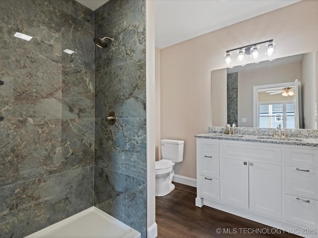 bathroom with toilet, wood finished floors, vanity, baseboards, and a tile shower