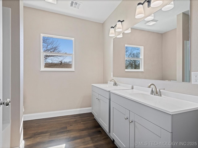 bathroom featuring a sink, wood finished floors, visible vents, baseboards, and double vanity