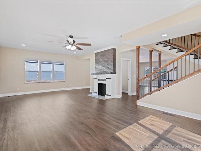 unfurnished living room featuring a large fireplace, stairway, dark wood finished floors, and visible vents