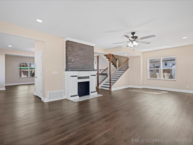 unfurnished living room with a fireplace, stairway, dark wood-type flooring, a ceiling fan, and baseboards