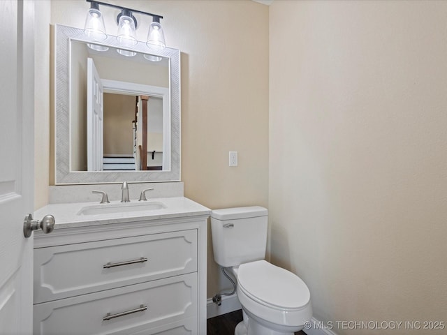 half bathroom featuring toilet, baseboards, and vanity