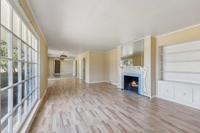 unfurnished living room featuring built in shelves, a high end fireplace, baseboards, ornamental molding, and light wood finished floors