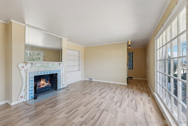 unfurnished living room featuring crown molding, a premium fireplace, a wealth of natural light, and wood finished floors