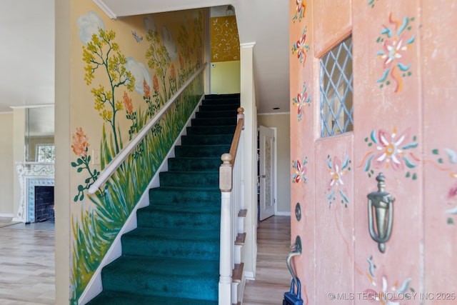 stairs with a fireplace, ornamental molding, wood finished floors, baseboards, and wallpapered walls