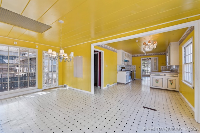 kitchen featuring baseboards, light floors, hanging light fixtures, stainless steel range with electric stovetop, and a notable chandelier