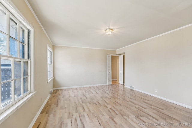 empty room featuring crown molding, light wood-style flooring, and baseboards