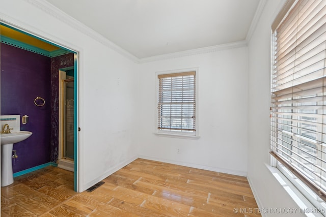 empty room featuring light wood-style floors, visible vents, ornamental molding, and baseboards