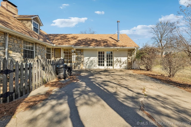 view of side of home featuring stone siding, a chimney, fence, and french doors