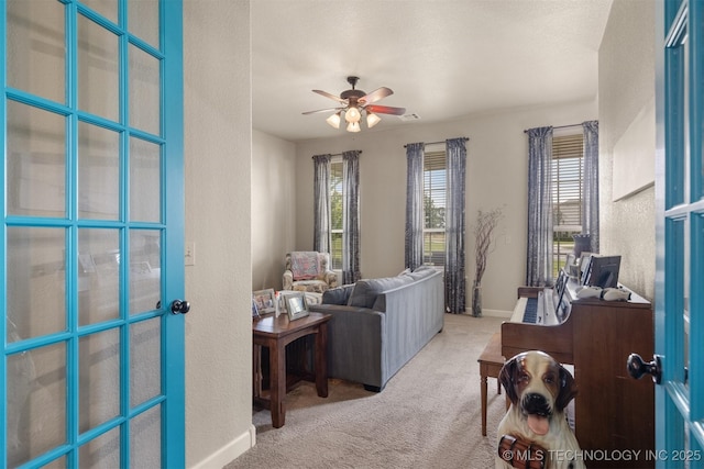 carpeted living area with baseboards and a ceiling fan