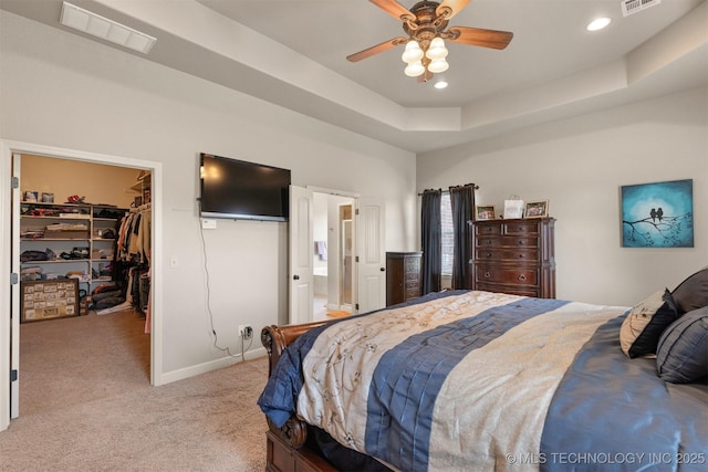 bedroom featuring a spacious closet, a tray ceiling, visible vents, and light colored carpet