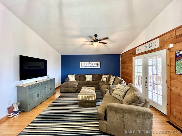 living area featuring french doors, vaulted ceiling, wooden walls, and light wood finished floors