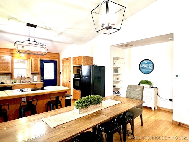 kitchen featuring tile countertops, backsplash, light wood-style floors, a sink, and black appliances