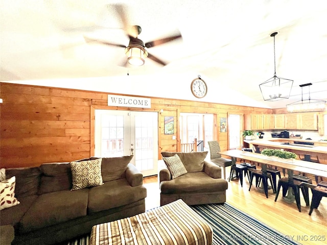 living area featuring lofted ceiling, wooden walls, wood finished floors, a ceiling fan, and french doors