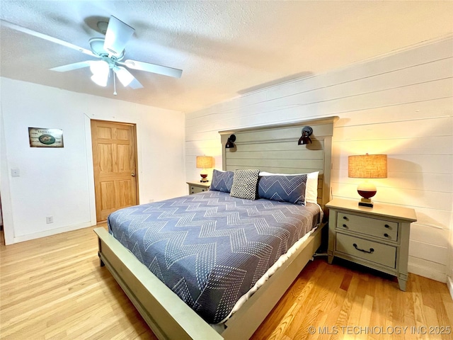 bedroom with a textured ceiling, ceiling fan, light wood-style flooring, and baseboards