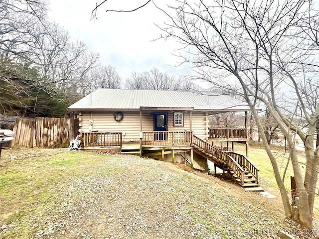 view of front of property with metal roof, gravel driveway, log siding, and fence