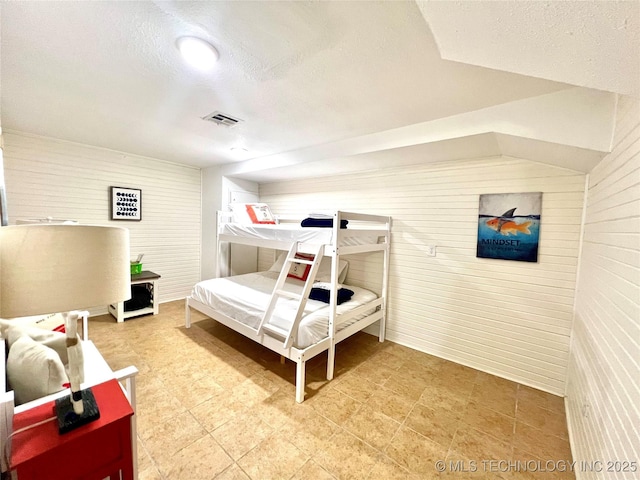 bedroom featuring wood walls, visible vents, and a textured ceiling