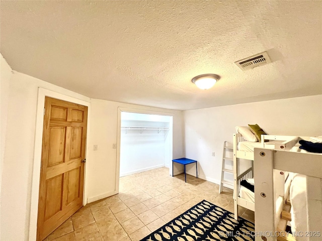 bedroom featuring light tile patterned floors, a closet, visible vents, a textured ceiling, and baseboards