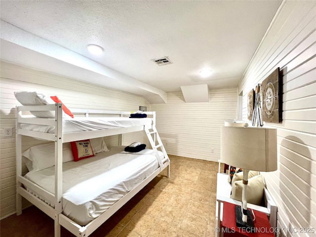 bedroom featuring a textured ceiling, visible vents, and wooden walls