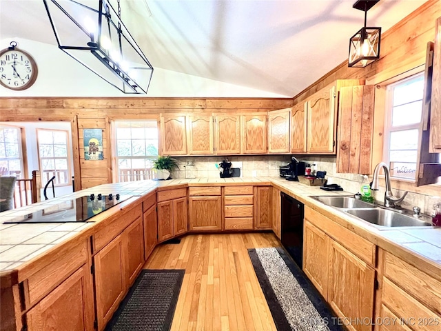 kitchen featuring tile countertops, light wood-style flooring, vaulted ceiling, a sink, and black appliances