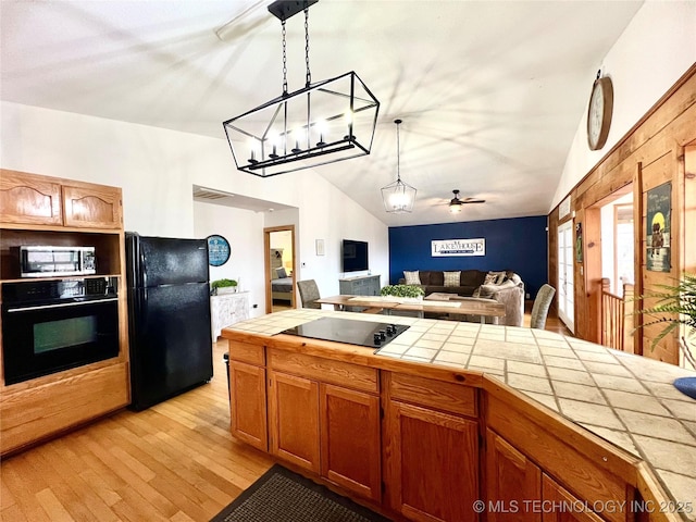 kitchen with tile counters, open floor plan, vaulted ceiling, black appliances, and pendant lighting