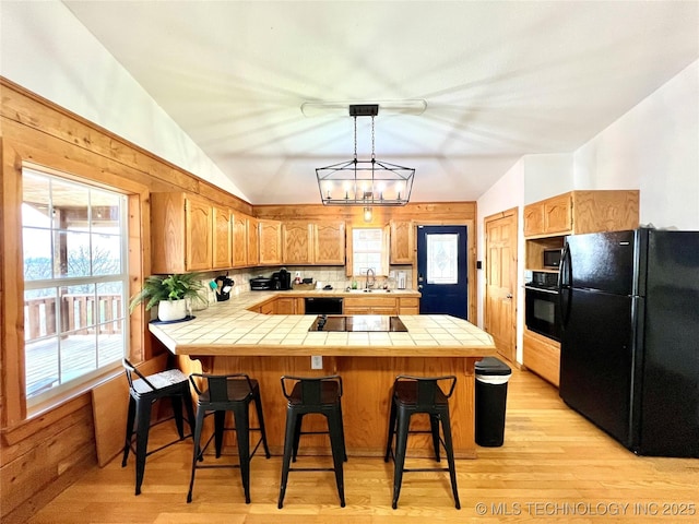 kitchen featuring black appliances, a peninsula, a sink, and tile counters
