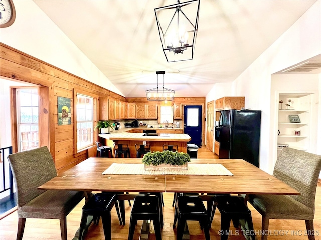 dining space with visible vents, vaulted ceiling, wood walls, built in shelves, and a notable chandelier