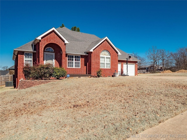 ranch-style house with fence, central AC unit, roof with shingles, a garage, and brick siding