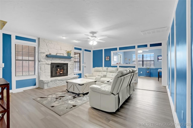 living area with a ceiling fan, visible vents, a stone fireplace, and wood finished floors