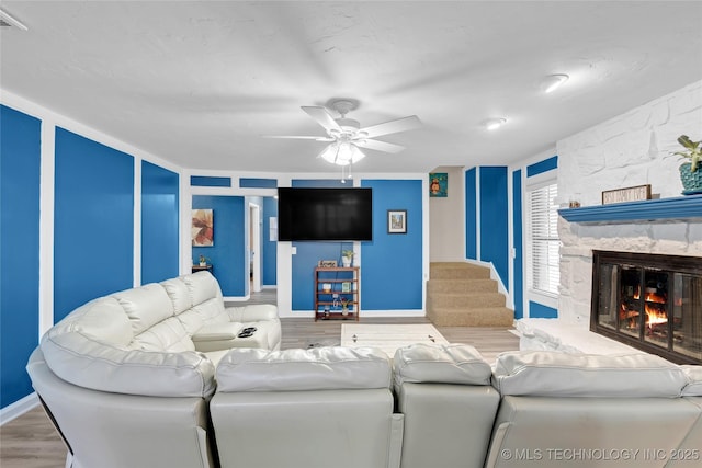 living area with baseboards, ceiling fan, stairway, wood finished floors, and a stone fireplace