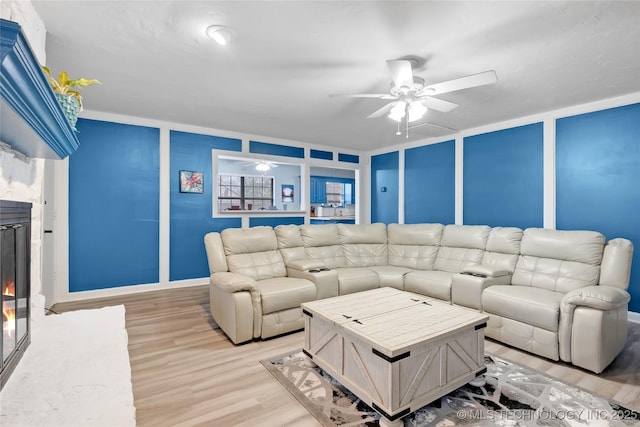 living room featuring light wood-type flooring, ceiling fan, a decorative wall, and a glass covered fireplace