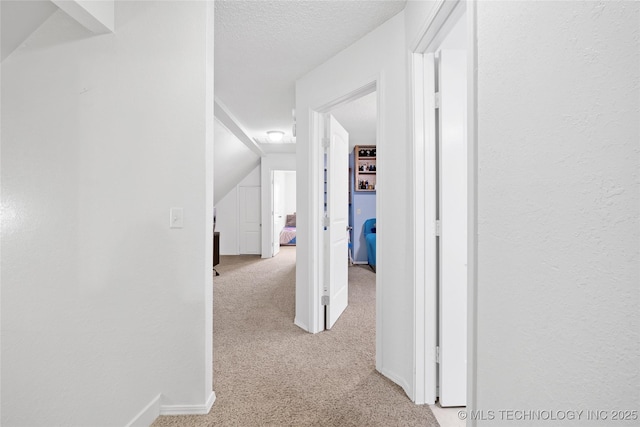 hall with light carpet, a textured wall, a textured ceiling, and lofted ceiling