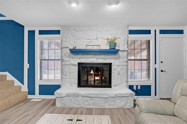 living area featuring a healthy amount of sunlight, stairs, wood finished floors, and a stone fireplace