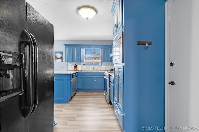 kitchen featuring light wood-style flooring, stainless steel appliances, a sink, blue cabinetry, and tasteful backsplash