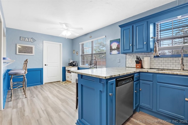 kitchen with a peninsula, a sink, blue cabinetry, dishwasher, and light wood finished floors