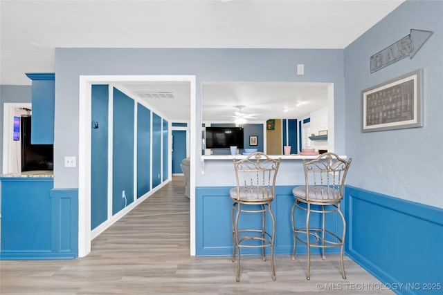 kitchen with visible vents, wainscoting, ceiling fan, light wood-style flooring, and freestanding refrigerator