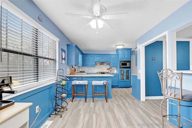 kitchen with tasteful backsplash, stainless steel microwave, blue cabinets, light countertops, and under cabinet range hood