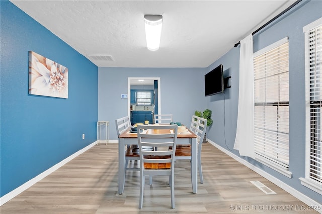 dining area featuring a textured ceiling, light wood-style flooring, visible vents, and baseboards