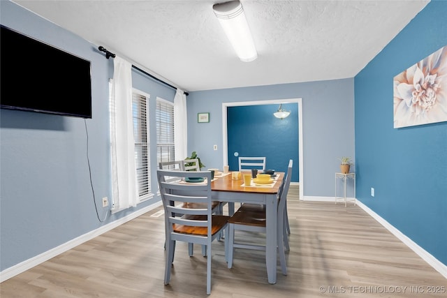 dining space featuring a textured ceiling, baseboards, and wood finished floors