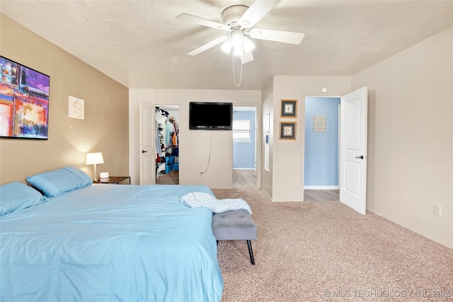 carpeted bedroom featuring a spacious closet, a closet, a ceiling fan, and baseboards