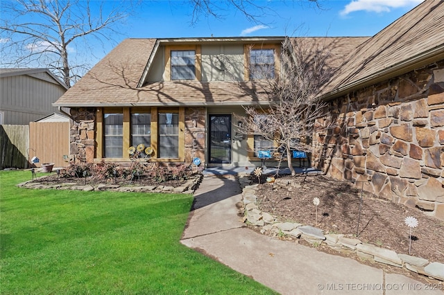 view of exterior entry with stone siding, a shingled roof, a lawn, and fence