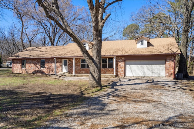 ranch-style home featuring dirt driveway, brick siding, cooling unit, and a garage