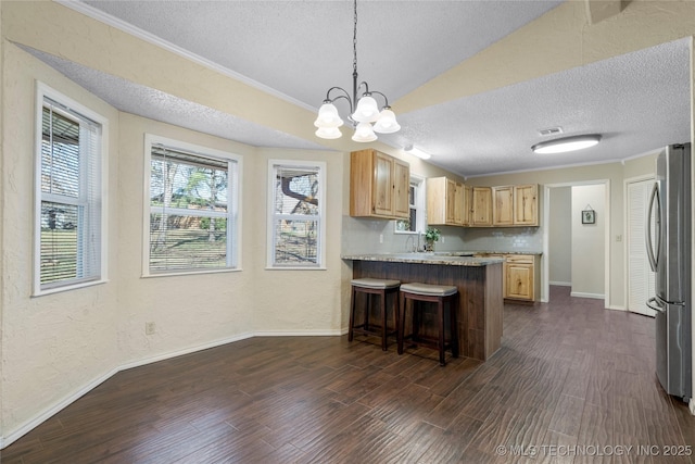 kitchen with a breakfast bar area, a peninsula, dark wood-style flooring, light countertops, and freestanding refrigerator