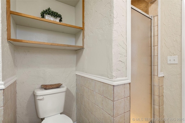 bathroom featuring a textured wall, a shower stall, and toilet