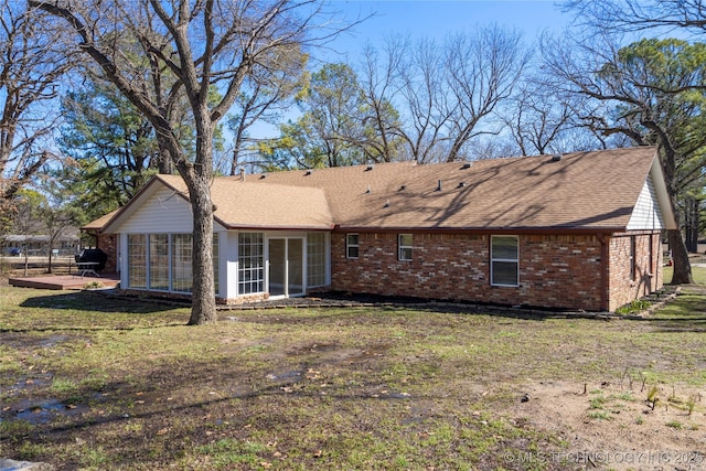 back of property with a shingled roof, a sunroom, brick siding, and a yard