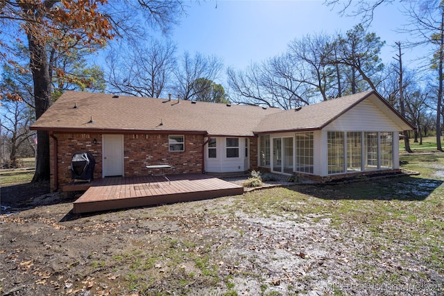 rear view of house featuring brick siding, roof with shingles, a wooden deck, and a sunroom