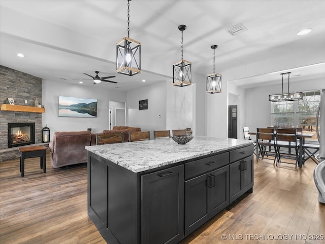 kitchen with visible vents, wood finished floors, dark cabinetry, a fireplace, and recessed lighting