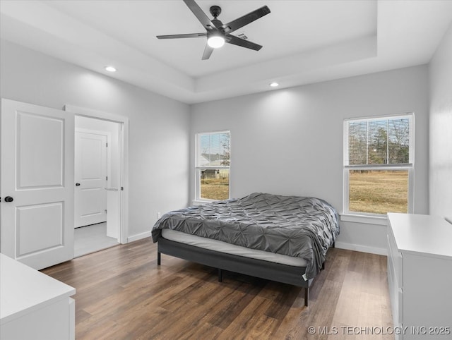 bedroom with wood finished floors, a raised ceiling, and baseboards